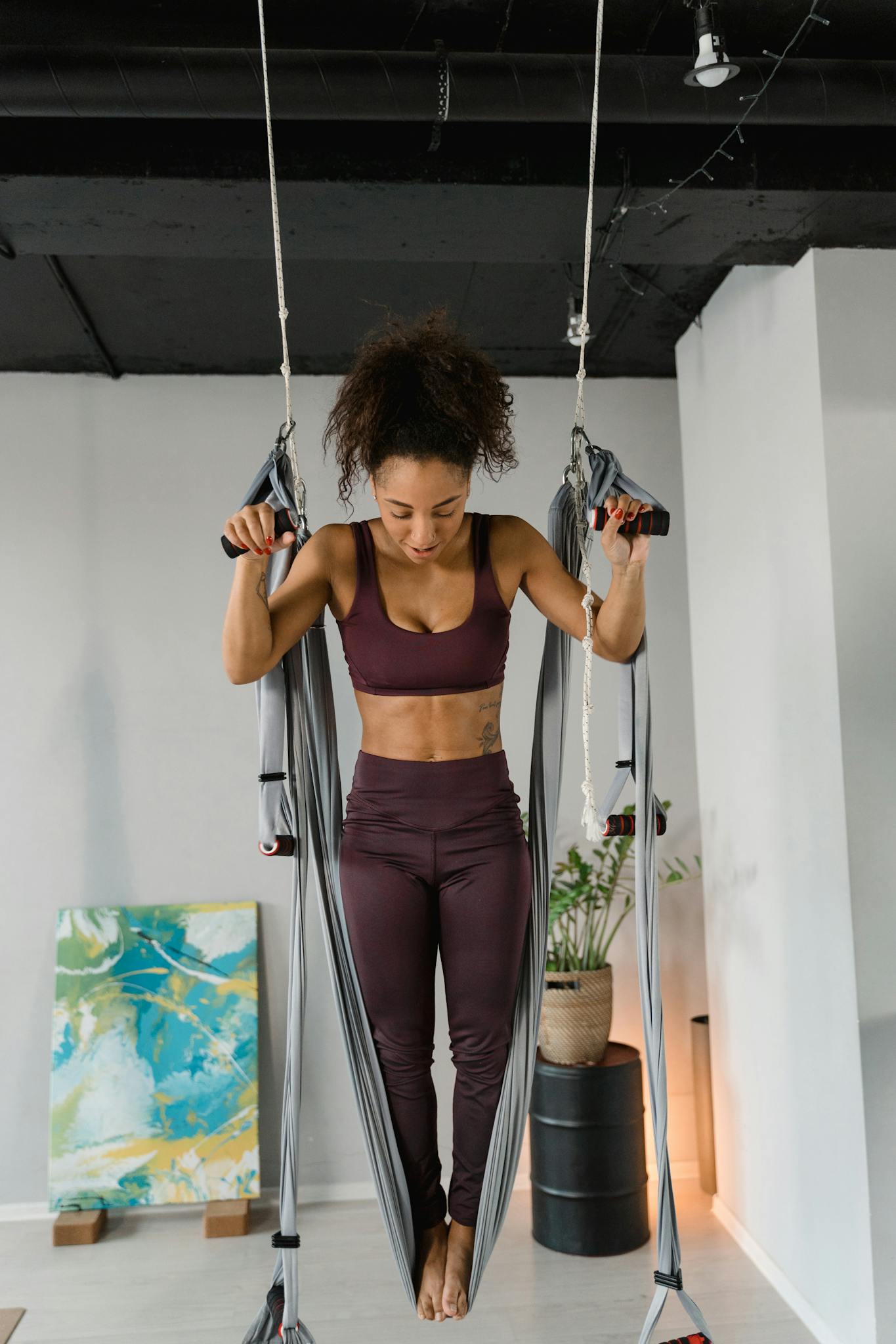 Fit woman engaged in an aerial yoga practice using a hammock setup in a modern studio.
