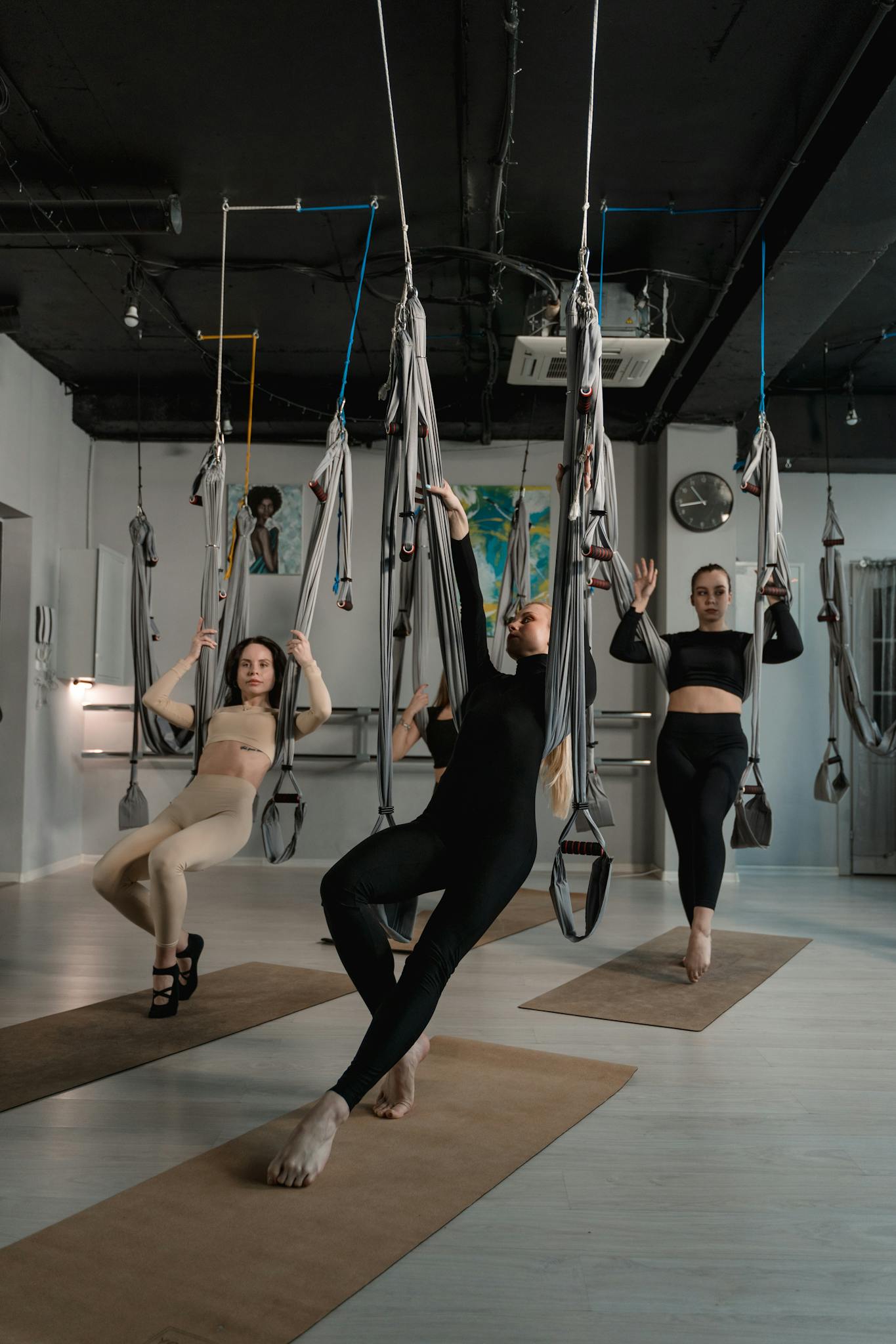 Group of women performing aerial yoga exercises in a well-lit studio setting.