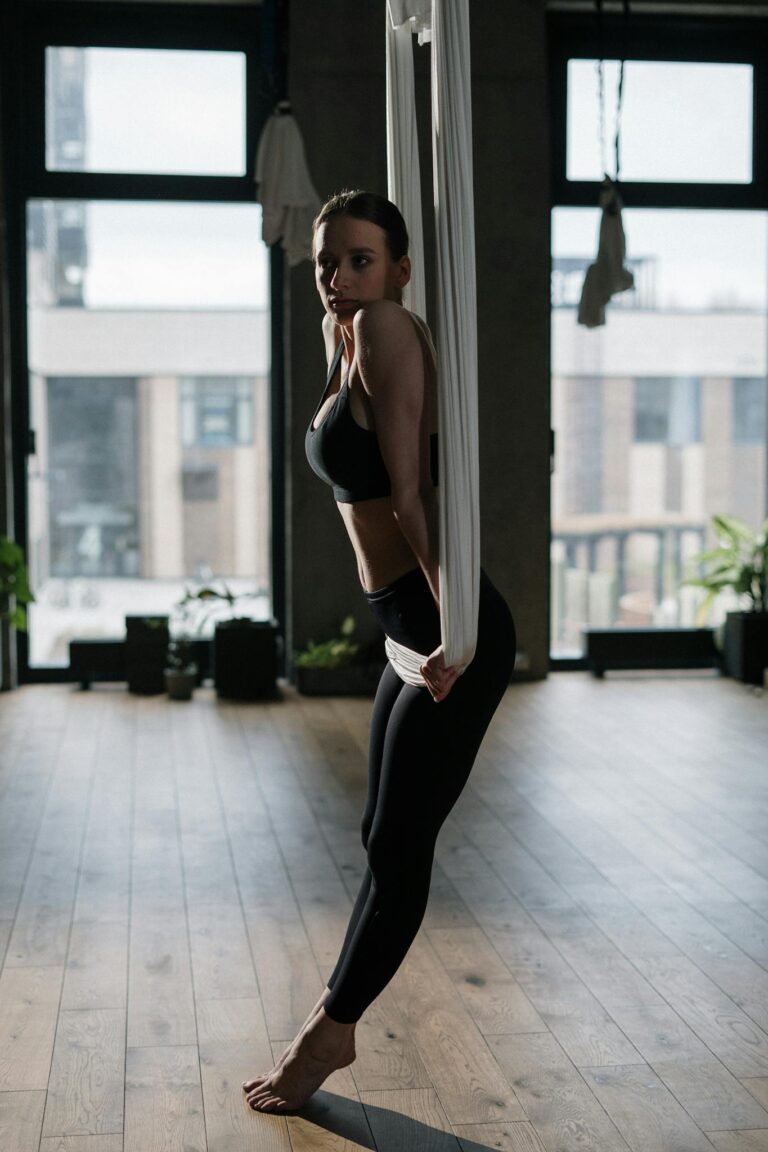 Woman practicing aerial yoga in a studio setting, focusing on balance and wellness.