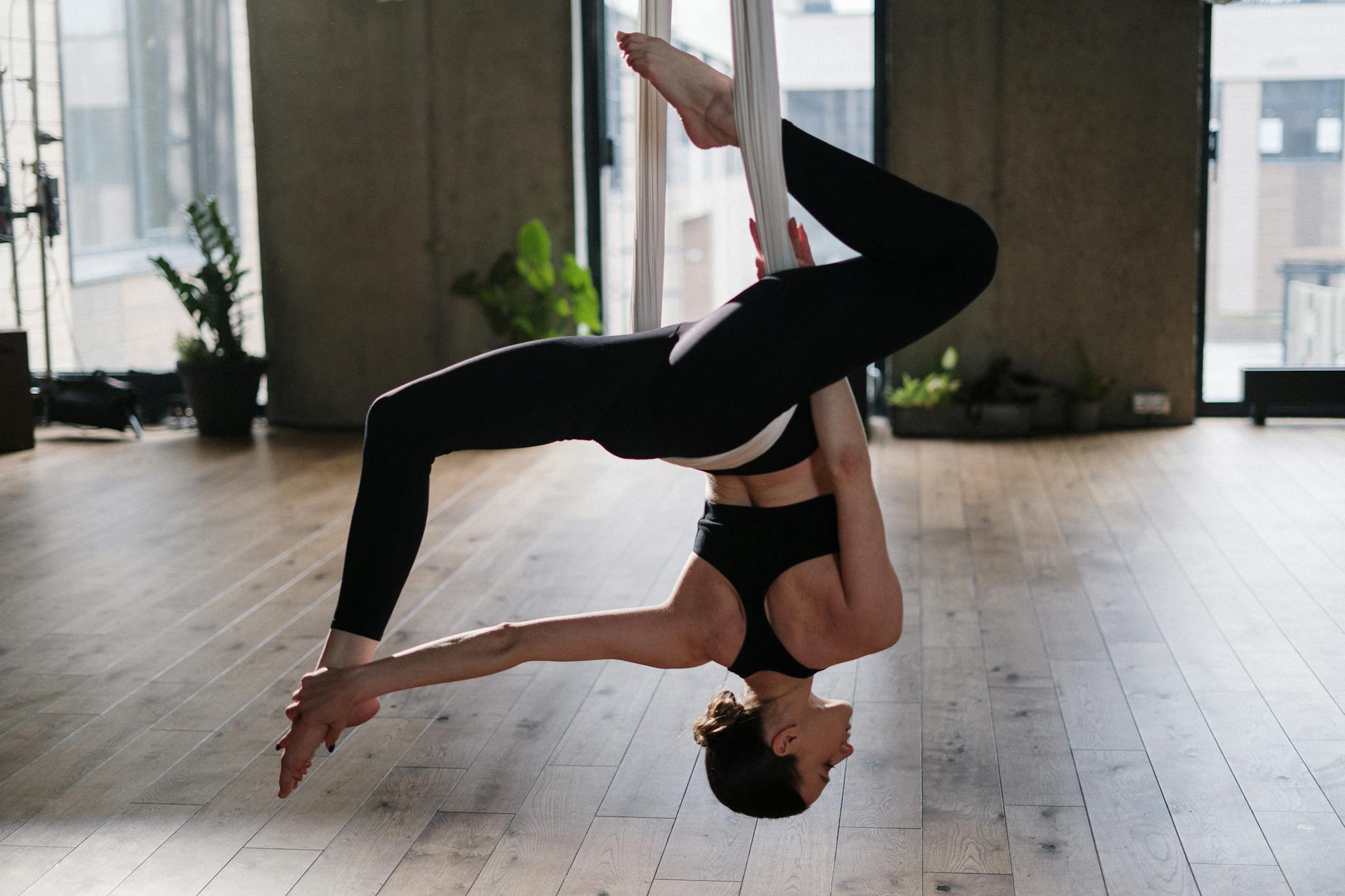 Woman practicing aerial yoga in a sunlit studio, showcasing balance and flexibility.