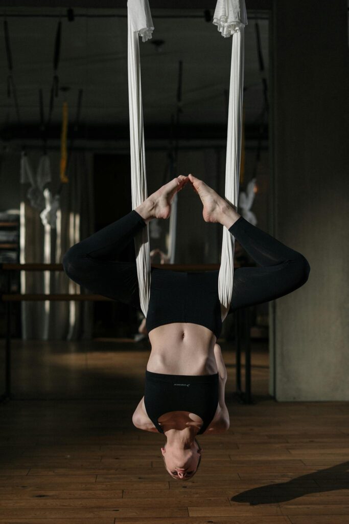 Woman practicing aerial yoga inversion in a well-lit, modern studio, promoting wellness and balance.